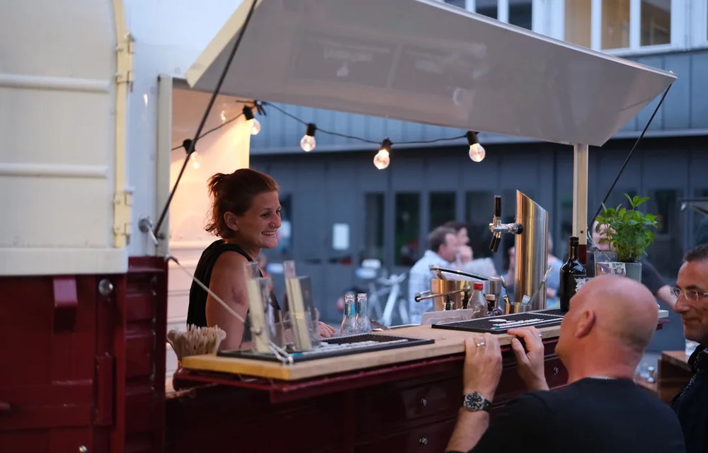 Mobile bar in a converted horse trailer at night, string lights and guests at the counter