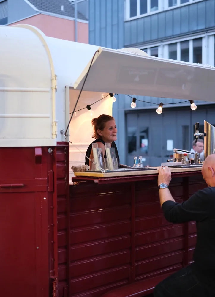 Mobile bar in a converted horse trailer, a barwoman serving and a guest at the counter